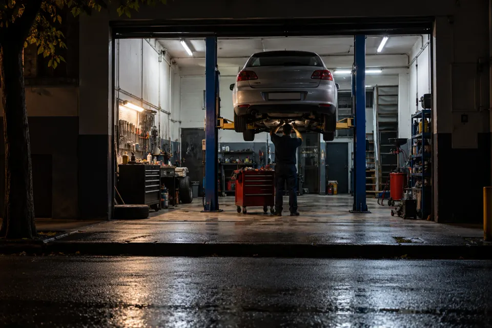 Taller mecánico iluminado de noche con un auto en el elevador